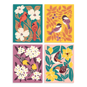 Grid of four colorful greeting cards each with a different illustrated design of two birds (chickadees, goldfinches, cardinals, and nuthatches) surrounded by leaves and flowers.