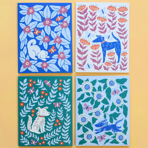 Four colorful greeting cards each with a different illustrated design of a dog surrounded by leaves and flowers illustrated by Chrissie Van Hoever.
