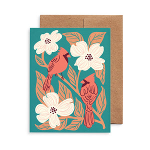 Illustrated greeting card with red cardinals and flowering dogwood on a pine green background.