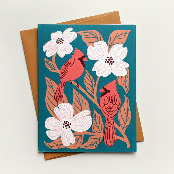 Illustrated greeting card with red cardinals and flowering dogwood on a pine green background.