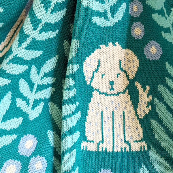 Close-up view of illustrated dogs and leafy fronds on a knit blanket