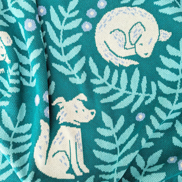 Close-up view of illustrated dogs and leafy fronds on a knit blanket