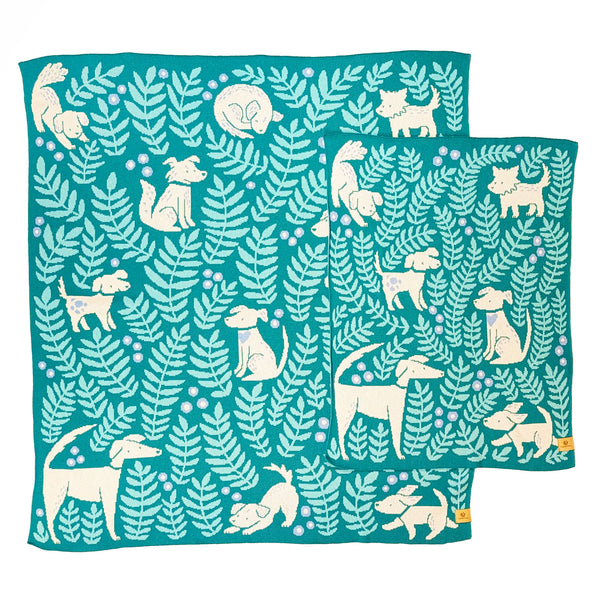 Crib and throw-size knit blankets illustrated with playful pups and leafy botanicals. The background color is a jade green with aqua leaves, light blue flowers, and cream-colored dogs of all shapes and sizes.