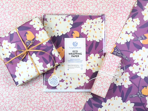 Package of the Goldfinch and Oleander wrapping paper surrounded by two wrapped gifts, each featuring a different side of the wrapping paper: one with the illustrated birds pattern, the other featuring the small flowers.