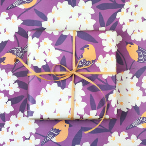 A gift wrapped in the Goldfinch paper featuring cheery yellow illustrated birds perched among bursting oleander blooms on a vibrant plum-colored backdrop.
