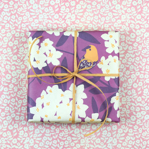 A gift wrapped in the Goldfinch paper on a backdrop of the reverse side of the paper featuring small cream and pink flowers.
