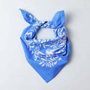 Cerulean blue and white organic cotton bandana neckerchief tied desperado-style illustrated with dancing mermaids, flowing kelp leaves, and fish.